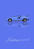 Be Anything You Want To Be – Blu art print: a blue Lamborghini Countach drawn flat in side profile, wedge shaped with a raised rear wing, mirrored quietly beneath the wheels, on a pale periwinkle ground, with the handwritten line Be anything you want to be! along the bottom