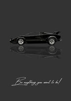 Be Anything You Want To Be – Nero art print: a black Lamborghini Countach drawn flat in side profile, wedge nose low and rear wing raised over the tail, doubled by a soft mirrored reflection beneath it, on a deep charcoal ground, with the handwritten line Be anything you want to be! underneath