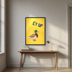 Ey Up Duck – Custard Gold art print in a black frame, styled above a desk