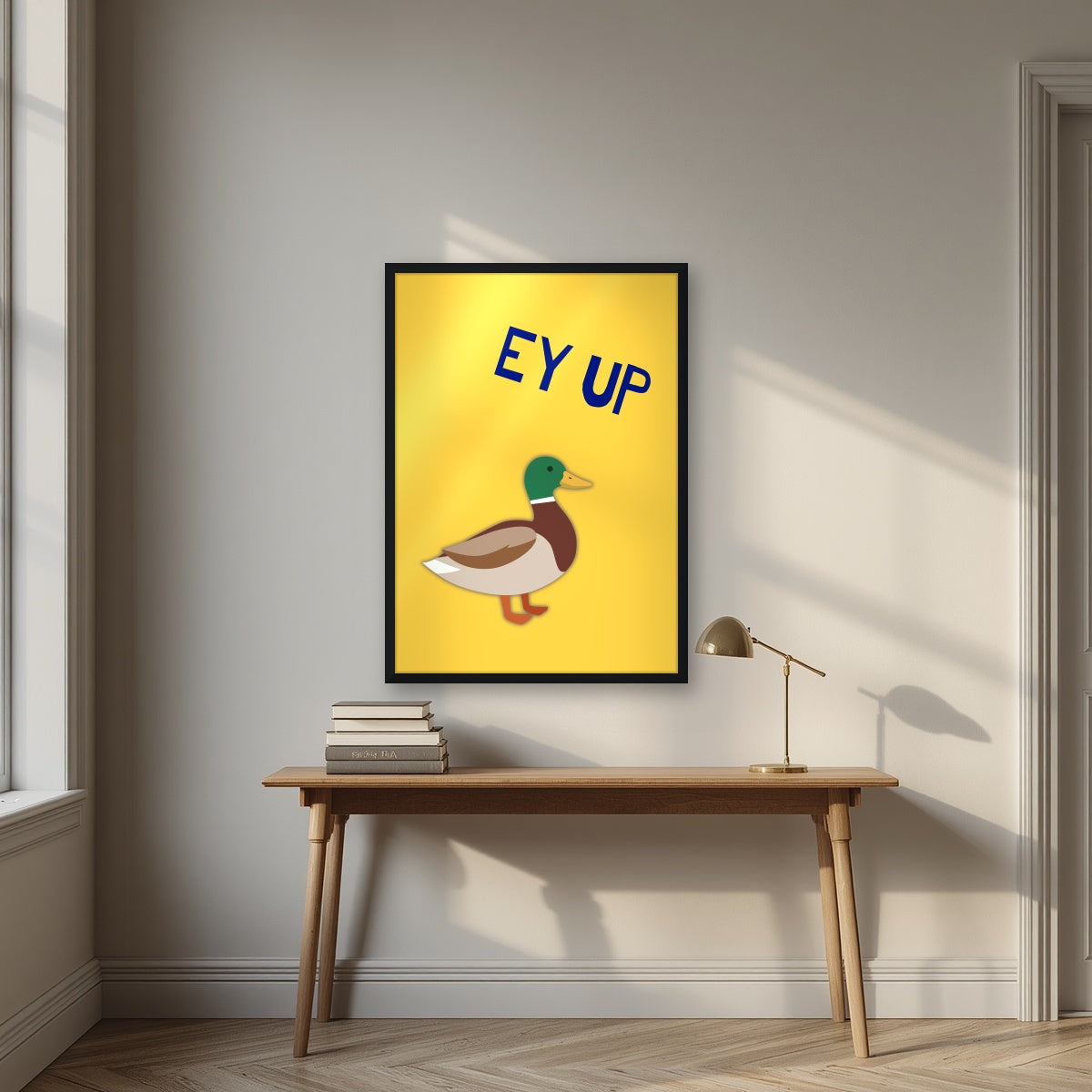 Ey Up Duck – Custard Gold art print in a black frame, styled above a desk
