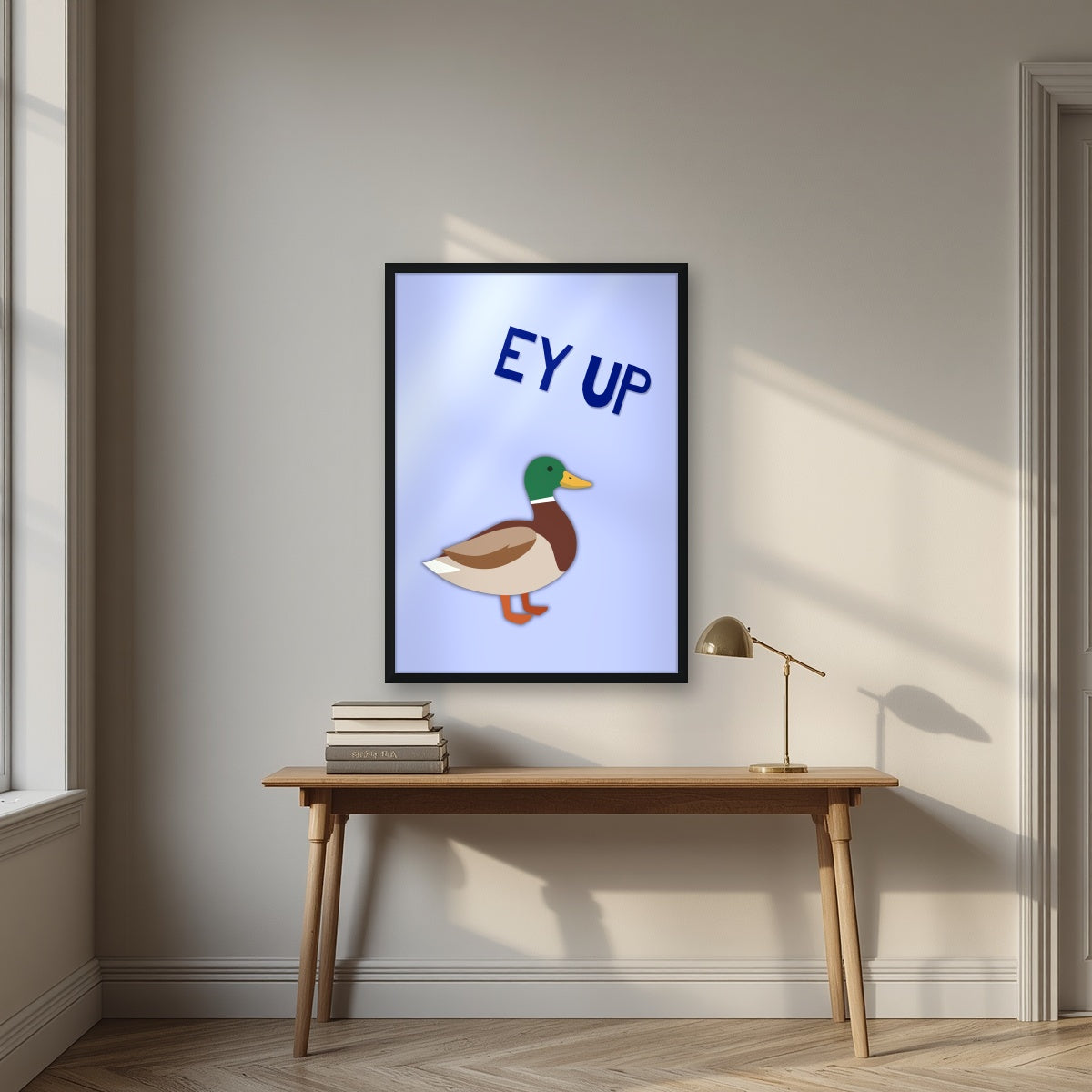 Ey Up Duck – Powder Blue art print in a black frame, styled above a desk