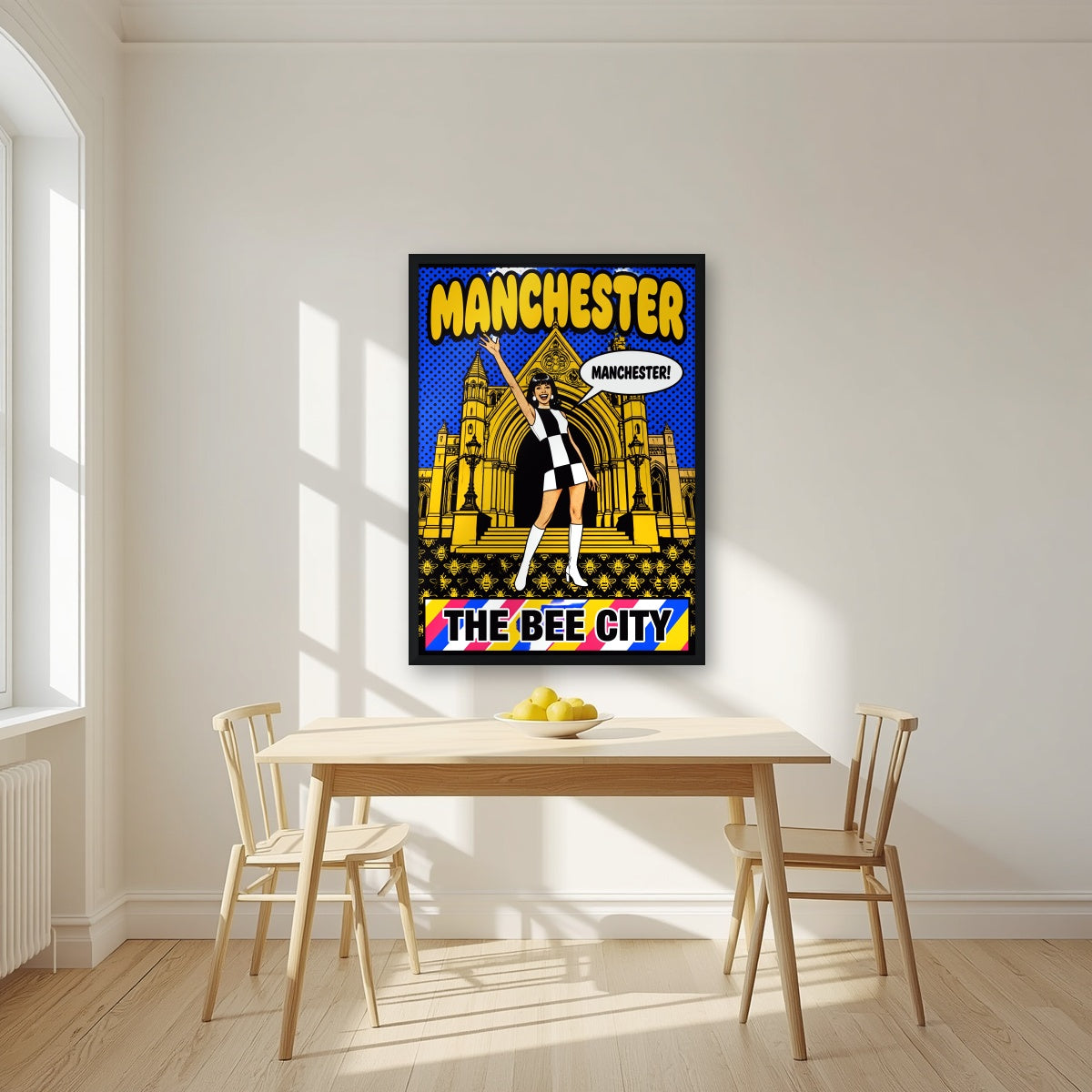 The Bee City Manchester art print in a black frame, above a dining table in a bright kitchen