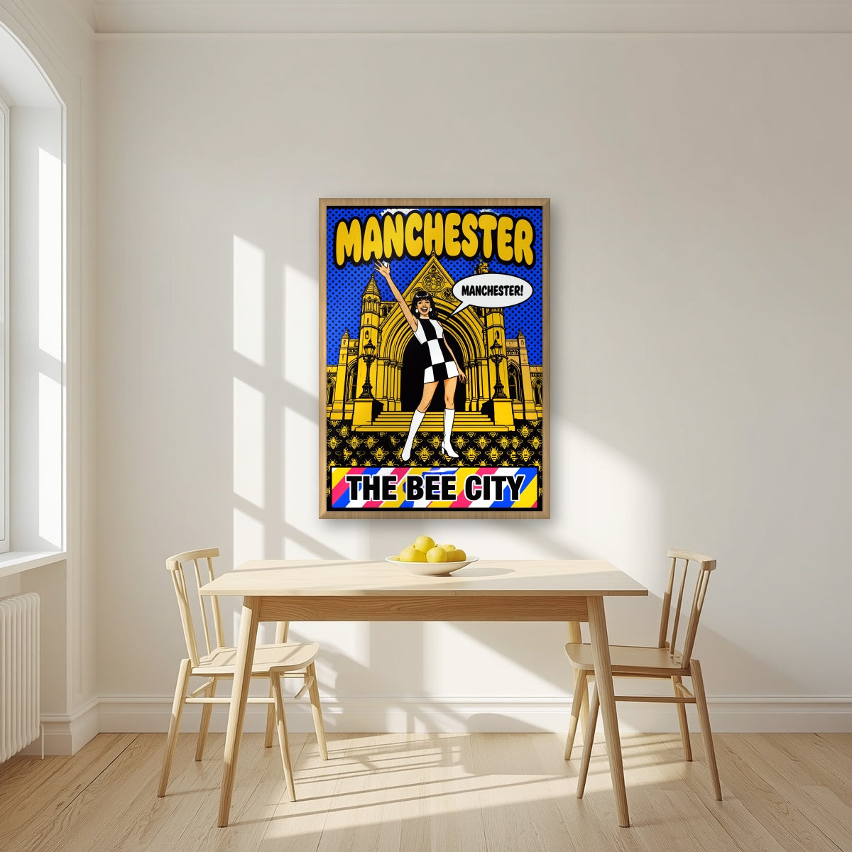 The Bee City Manchester art print in an oak frame, above a dining table in a bright kitchen