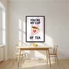 You're My Cup of Tea – Positano Pink in a black frame, above a dining table in a bright kitchen
